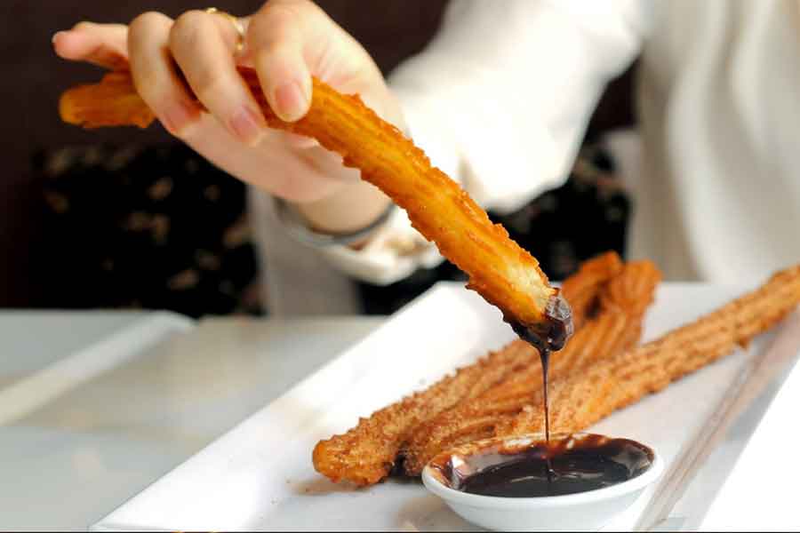     Query successful

Gemini said

A close-up of a hand dipping a long, golden-brown churro into a small bowl of thick, dark chocolate sauce. Several other churros rest on a white rectangular plate in the background. Enjoying this classic treat at a local café is one of the most delicious Spanish traditions to experience.