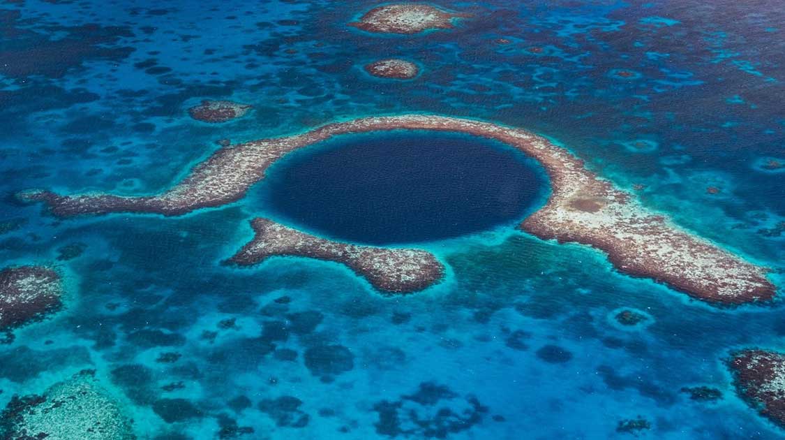 the great blue hole in belize. an underwater sinkhole surrounded by a reef in the middle of the blue ocean. this article tells you everything you need to know and why you should dive belize blue hole.