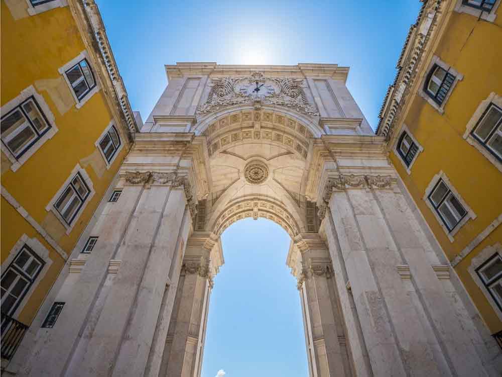 Arco de Rua Augusta, an iconic triumphal arch with clock located in Lisbon, Portugal, and yellow buildings on each side on a sunny day.