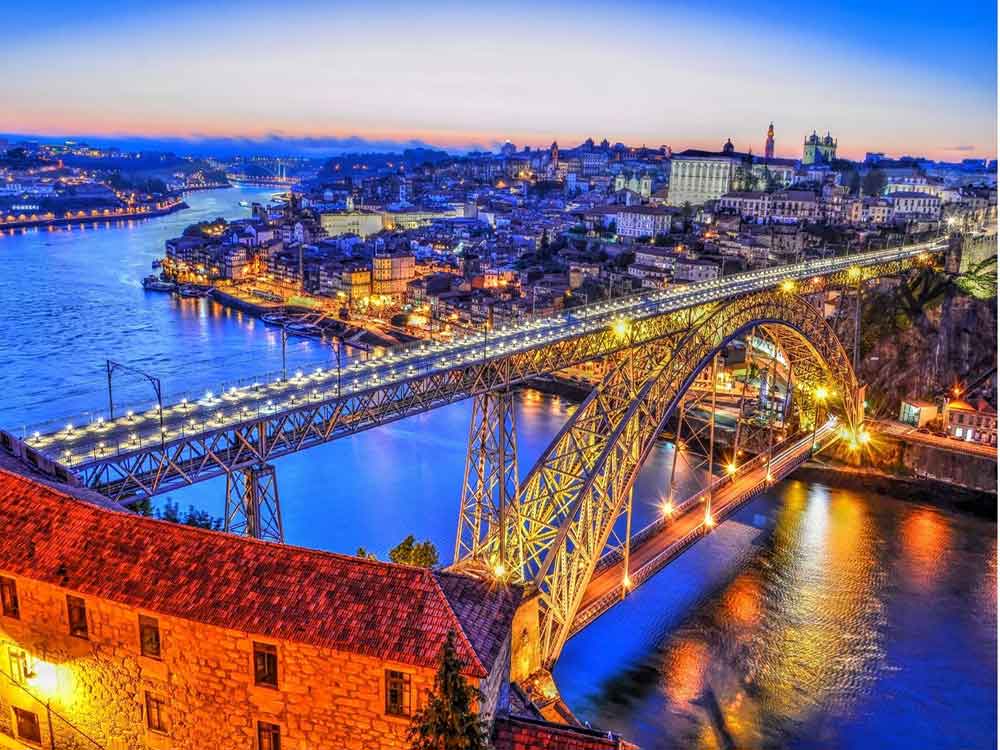 
Dom Luis Bridge in Porto, the famous double-decked iron arch bridge, is illuminated on an evening night, offering a view of the waters and the city.