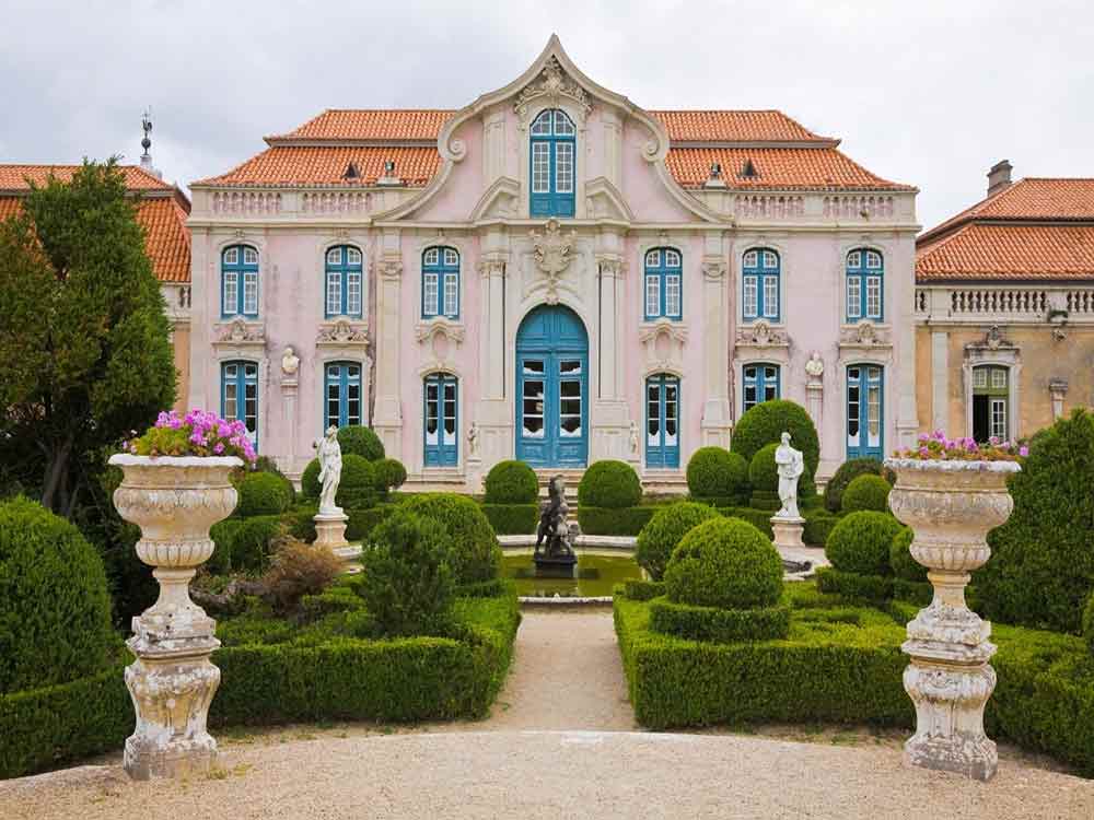 Queluz National Palace features blue windows and doors with a red-orange roof, all set against a well-manicured garden at the front.