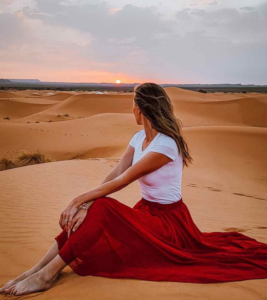 glamping in the sahara early morning with a woman in a red skirt and white top looking out to the desert