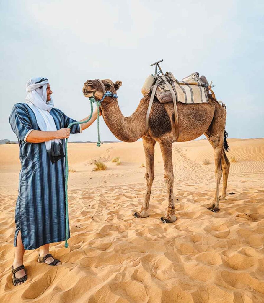 A man wearing a blue striped robe and white turban with a camel