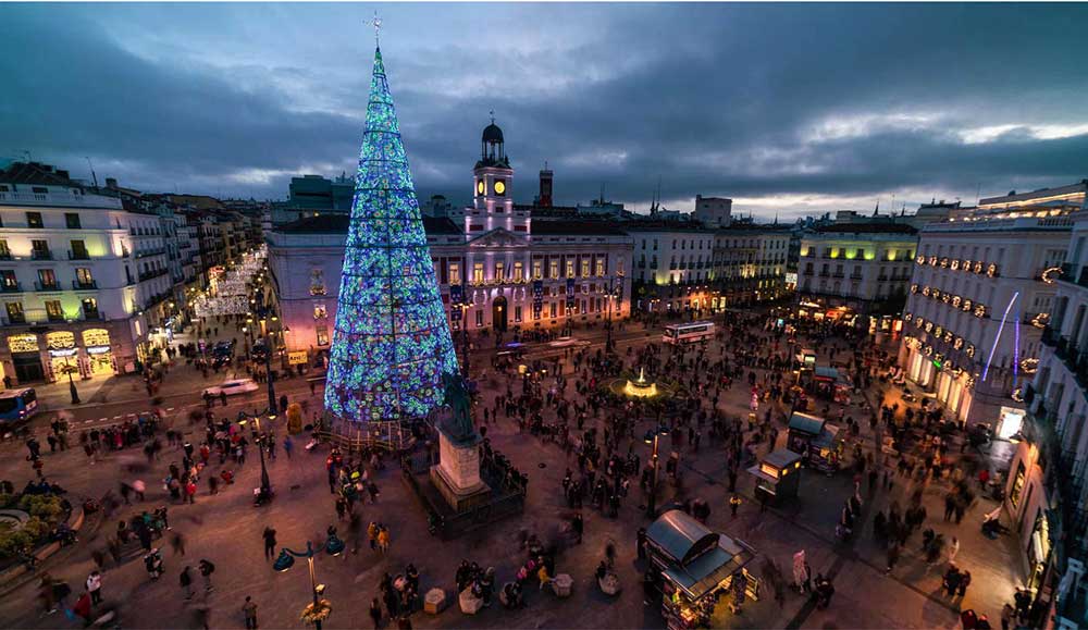 Madrid In Winter: Over 30 Things to Do In Winter in Madrid 8 Plaza Major at christmas showing a large tree in the centre with blue lghts and small christmas markets.