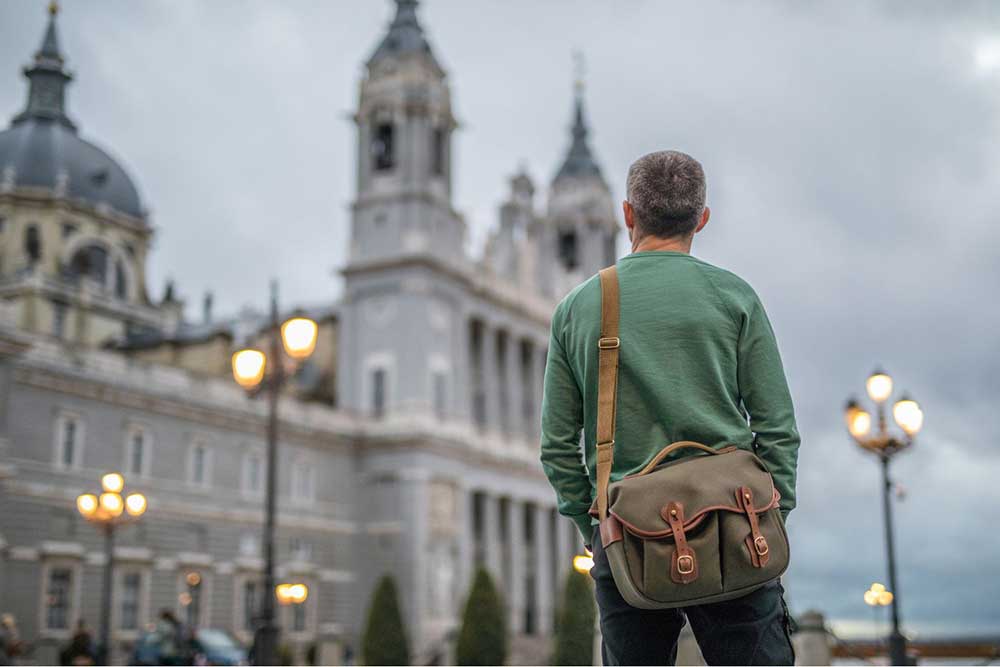 Madrid In Winter: Over 30 Things to Do In Winter in Madrid 5 A man standing in front of the Royal Palace in Madrid. He's wearing a green jumper and carrying a born bag over his sholder.