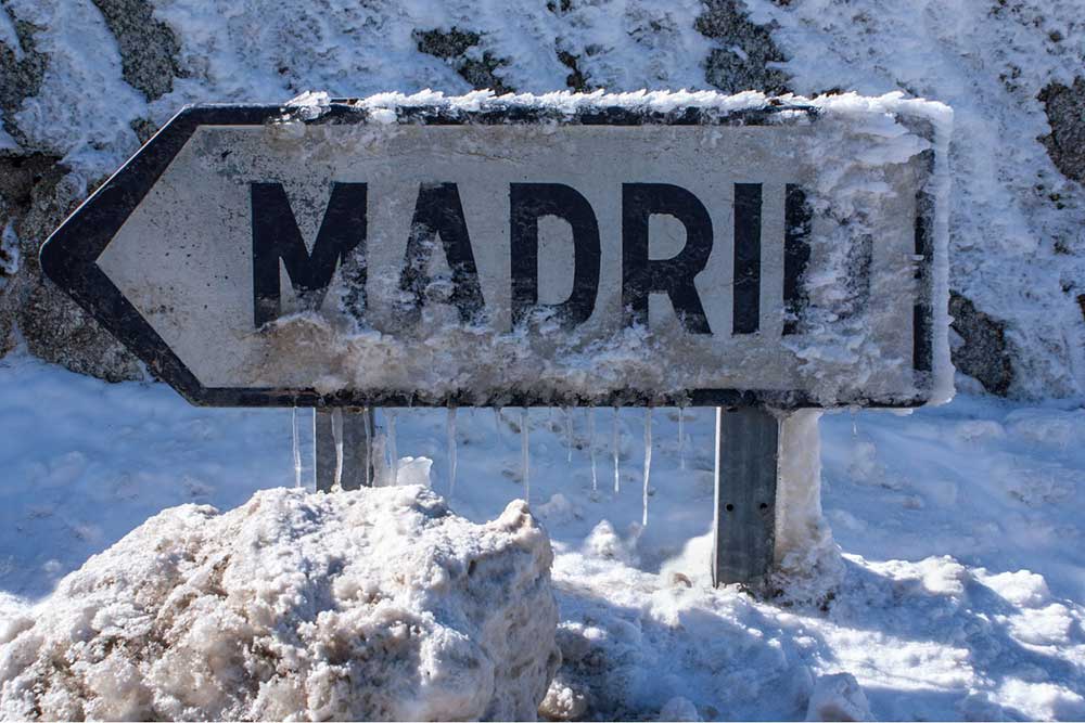 A road sign that reads Madrid, covered in snow and icicles.