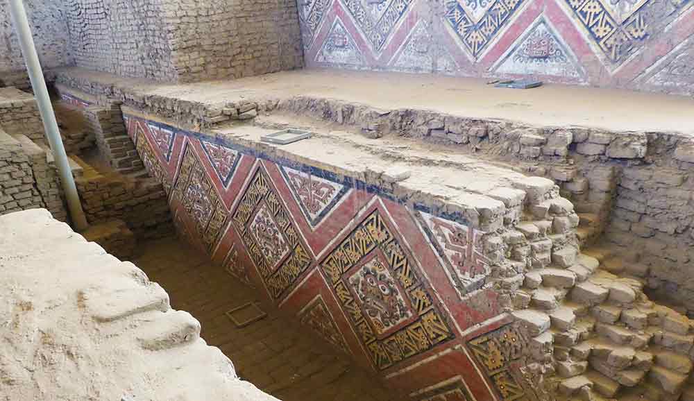 Painted murals of ornate faces in a diamond shaped motif on the walls at Huaca de la Luna ruins. 