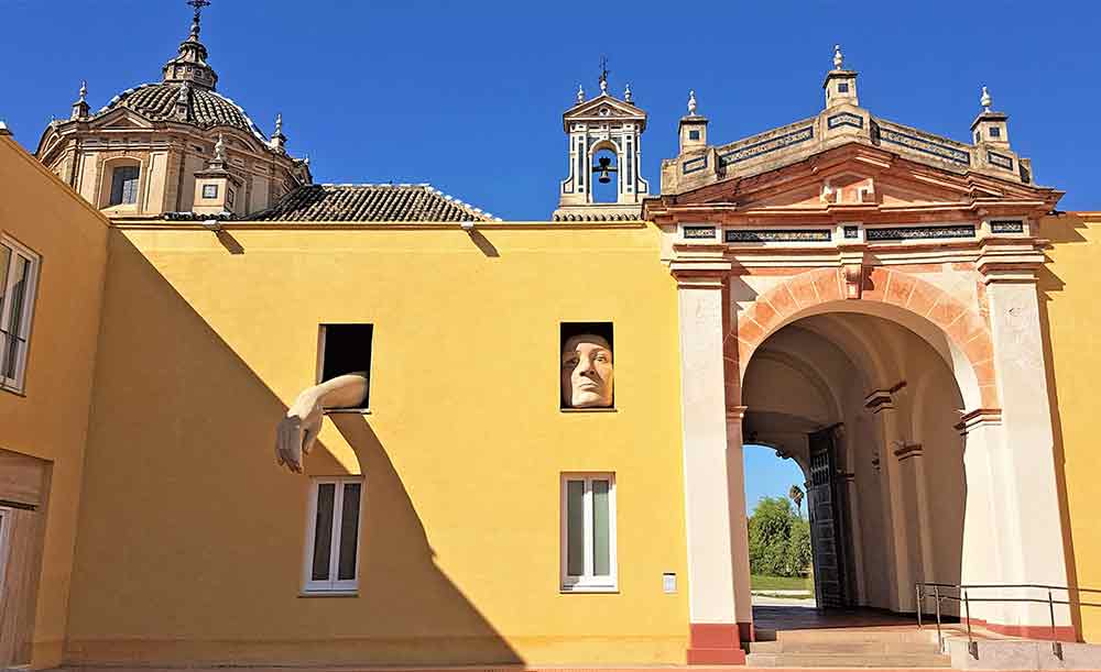 The "Alicia" art installation at the Centro Andaluz de Arte Contemporáneo (CAAC) in Seville, featuring a giant, whimsical sculpture of a girl's face and arms appearing to emerge from the brick walls of an old monastery. This striking contemporary piece is one of the most unique artistic sights to discover in Seville.
