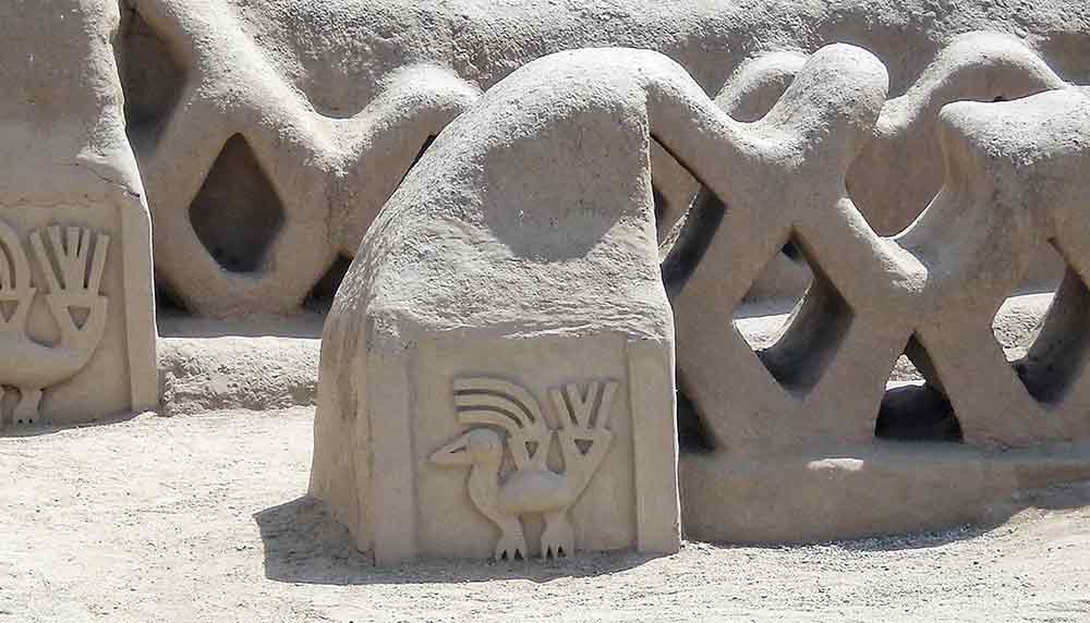 A small white block with a carving of a bird attached to a wall with a lattice like strcture at chan chan ruins. 