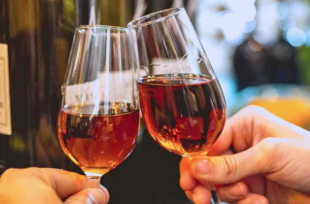 A close-up of a small glass of Vino de Naranja (orange wine) alongside a traditional tapa of Manchego cheese, served on a classic wooden bar counter. Sampling this sweet, citrus-infused local speciality is one of the most authentic gastronomic highlights in Spain for any food lover.