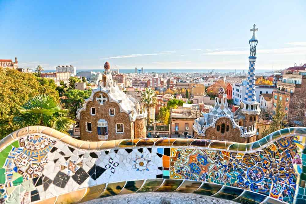 Colourful mosaic bench overlooking whimsical buildings in Park Güell, Barcelona—an architectural highlight and must-see attraction in Spain.