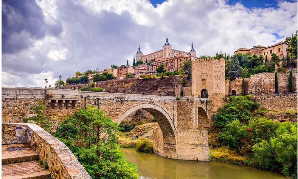 Puente de San Martín leading to the fortified city of Toledo, with the Alcázar rising in the background—an essential stop on many heritage tours of Spain.