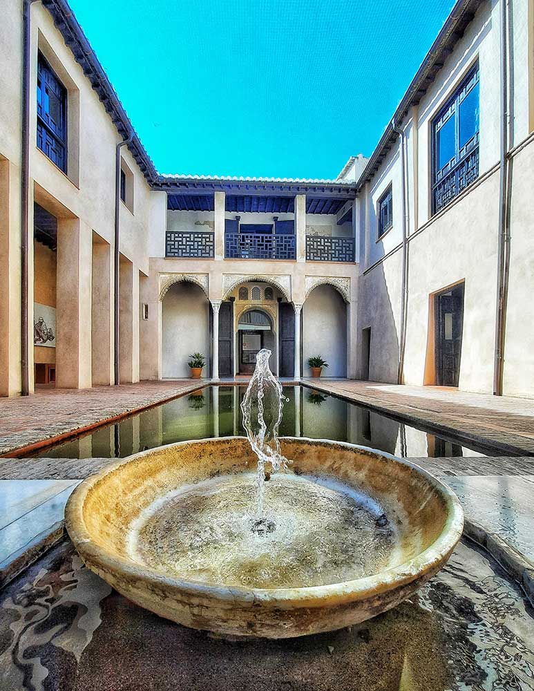 Fountain at its center surrounded by light brown buildings on a sunny day