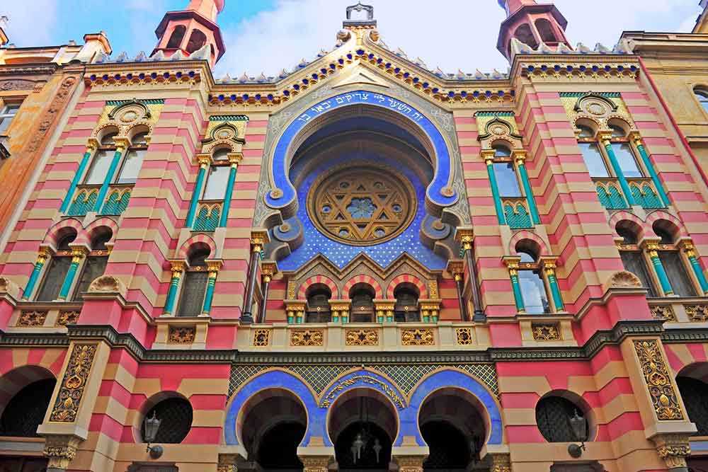 A colourful Synagogue in Prague with red and yellow striped bricks and a blue archway. 