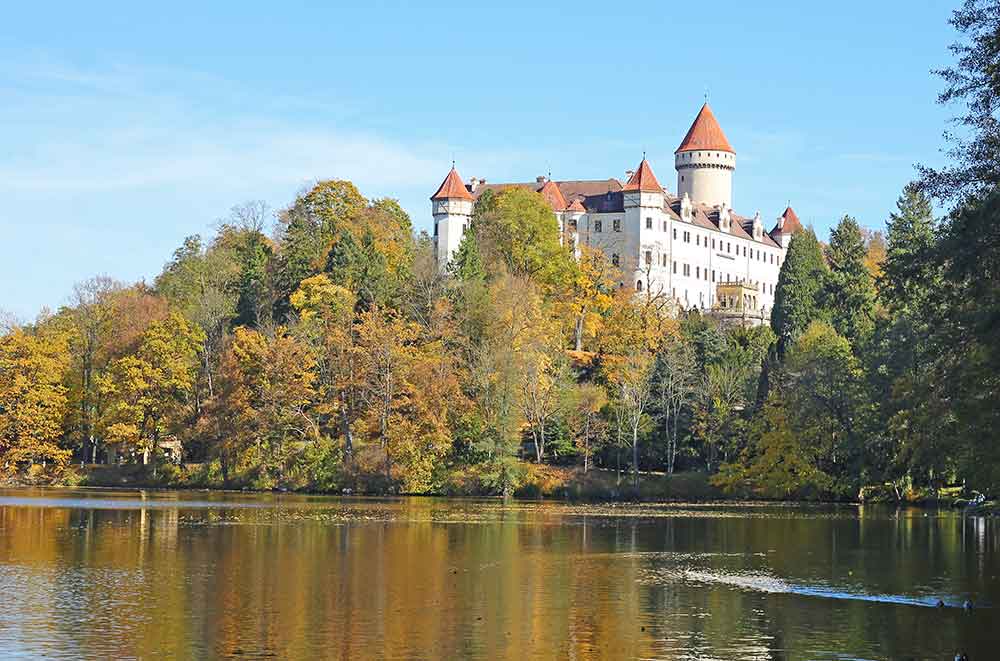 Konopiste Castle on a lake surrounded by autumn coloured trees. 