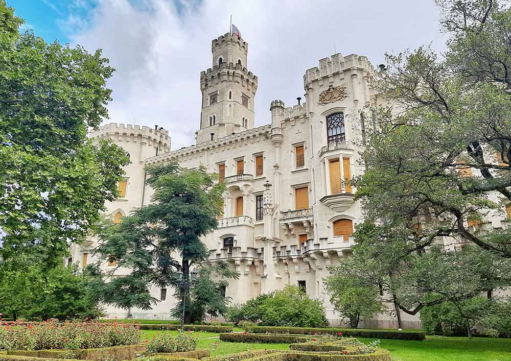 Chateau Hluboka with pale coloured stone building with turrets in gardens.