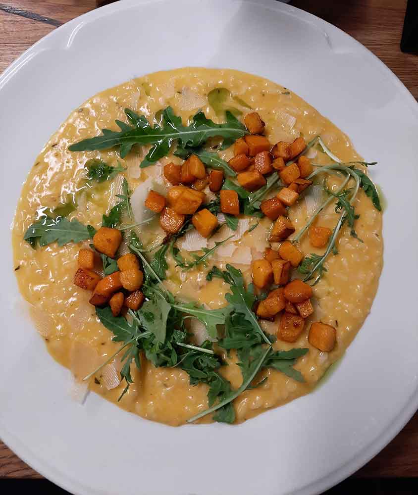 A plate of pumpkin risotto with rocket and parmesan on top.