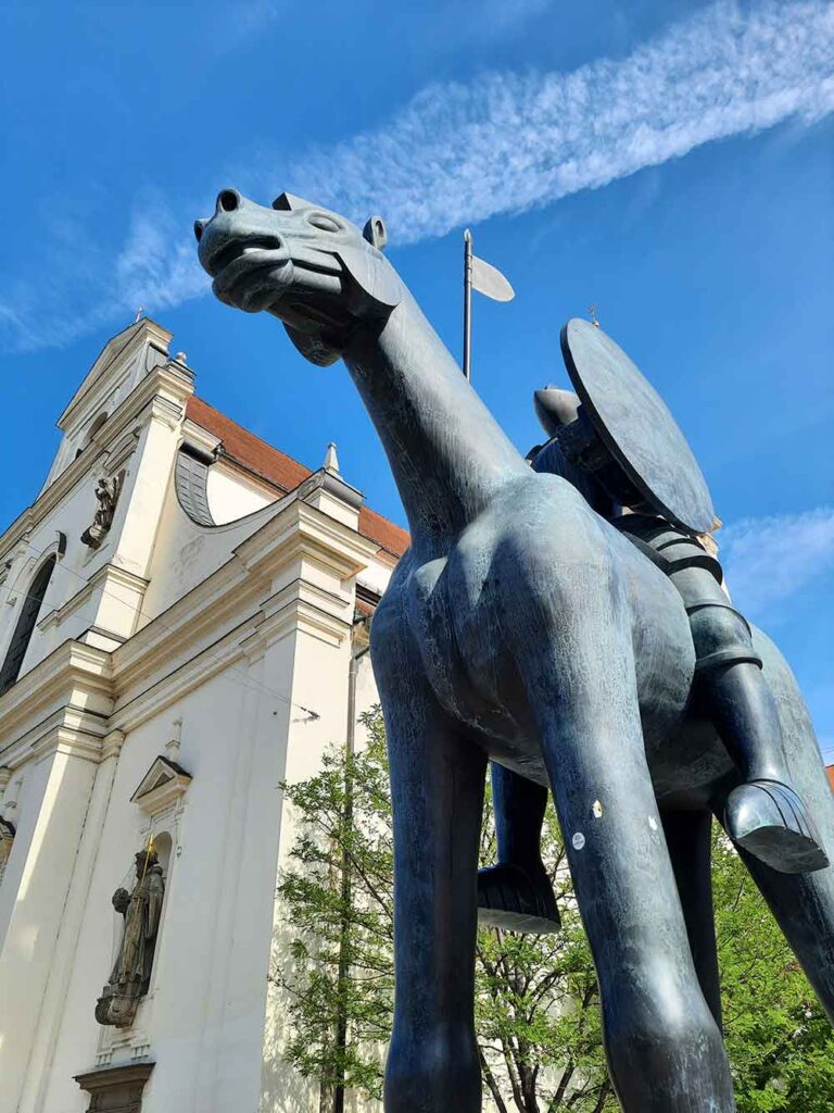 The Brno Horse and Knight statue in front of a church with blue skies in the background. 