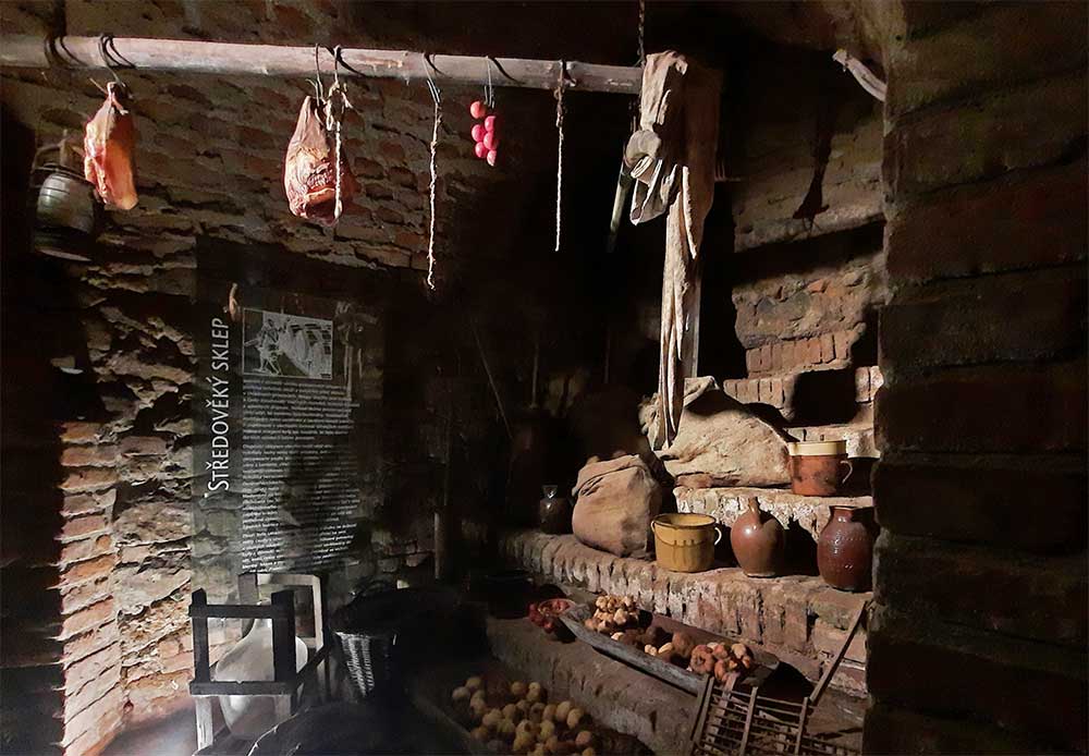 One of the caverns inside Labyrinth Under The Vegetable Market in Brno with produce hanging from the ceiling and on shelfs.
