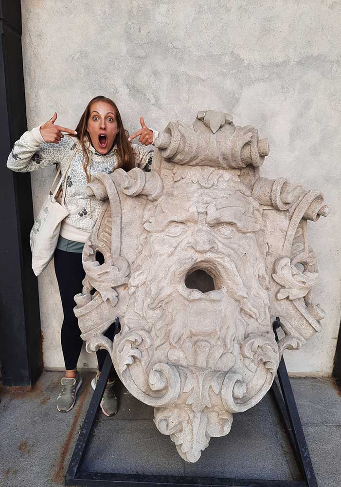 A woman (me) stood next to the The original statues from the Samson fountain pulling a silly face to mimic the statue.