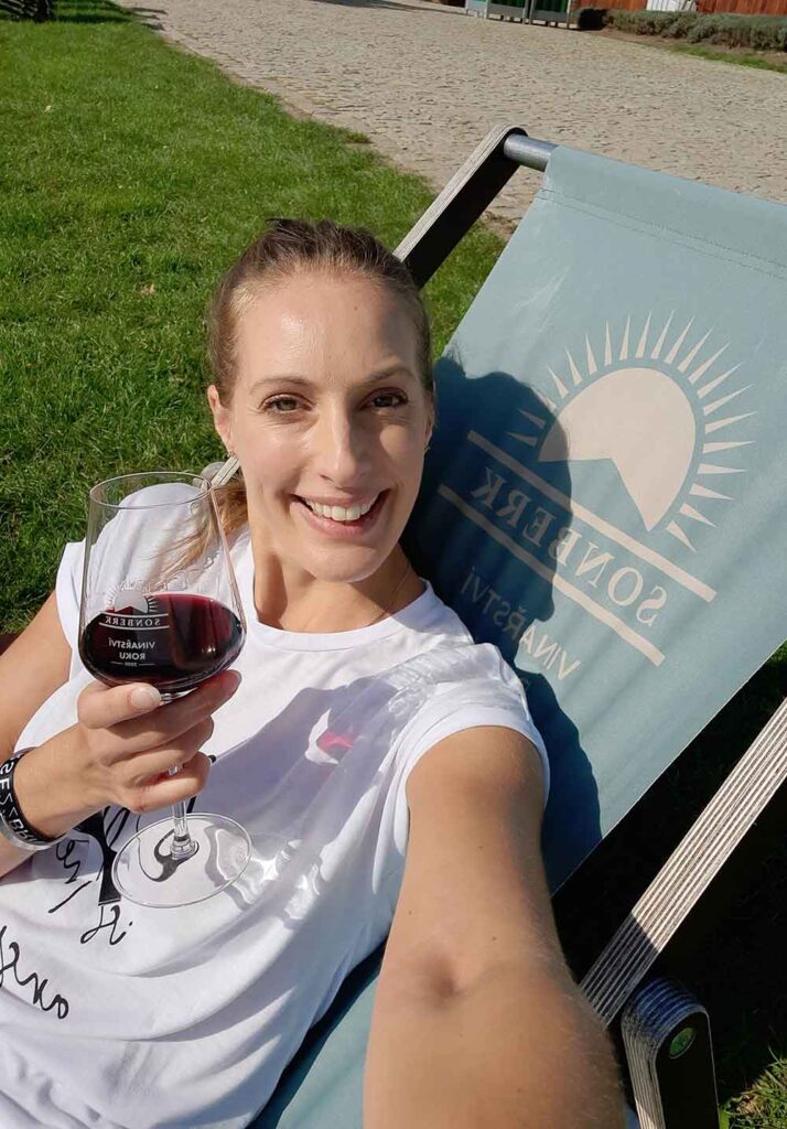 How To Visit 3 Vineyards Near Brno On An Easy Self-Guided Wine Tour, Czech Republic 7 A woman (me) sat in a desk chair at Sonberk winery drinking a glass of red wine.