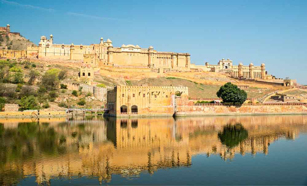 Amer Fort Palace in India sitting on a hill featuring sandstone walls with an overlooking Maota Lake
