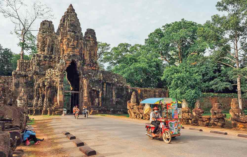 The Angkor Archaeological Park in Cambodia features an ancient arch as the entrance to the park, with lined statue ruins.