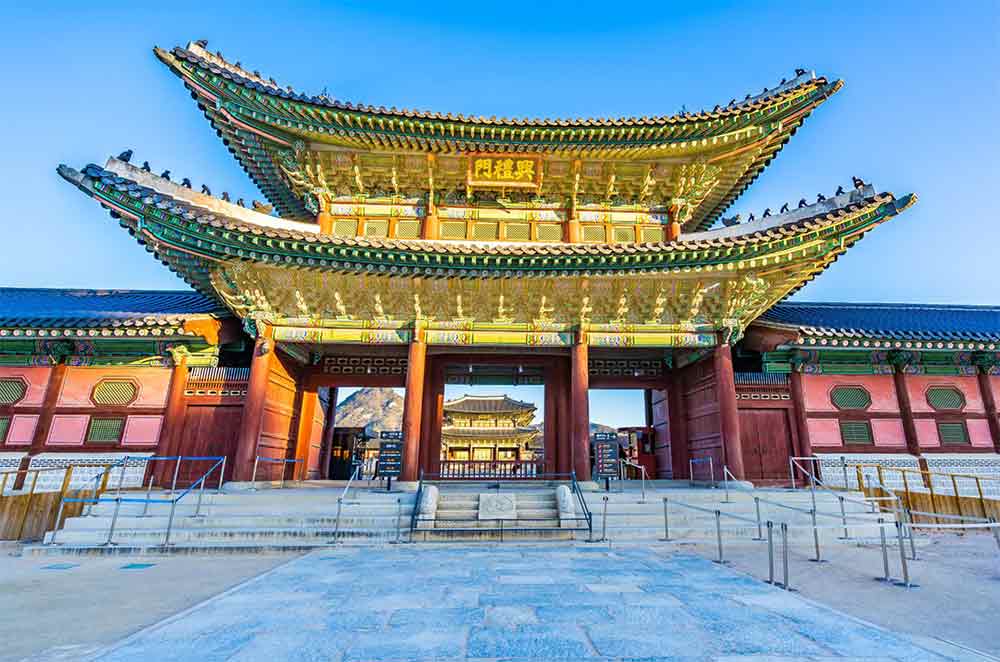 Gyeongbokgung Palace in Korea showcases its grand entrance with yellow two-tiered roof in a clear blue sky