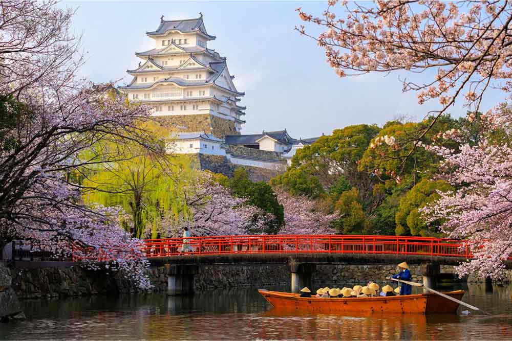 Himeji Castle in Japan features a multi-tiered roof, and from its premises, you can enjoy a view of the lake with a red bridge.