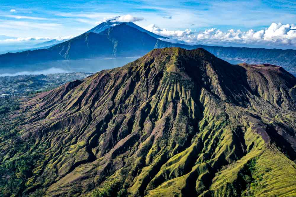 Mount Batur in Bali, Indonesia, is an active volcano with lush green surroundings set against a clear blue sky.