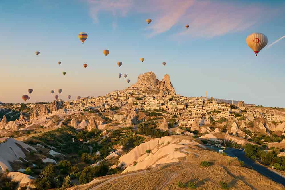An aerial view of Cappadocia & Uchisar Castle in Turkey featuring geological formations and hot air balloon rides with a natural rock formation castle and small houses
