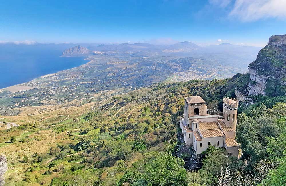 A castle like building perched on a hillside over looking trees and valleys and out to the sea in sicily. But where is Sicily located? find out in this article. 