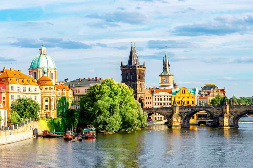View of Charles Bridge in Pague from the River with buildings on the river bank.