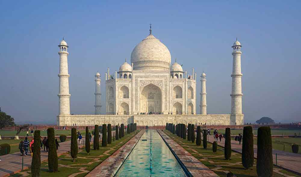 Taj Mahal in India with its pristine white marble construction with a grand central dome at the center and well maintain gardens at front