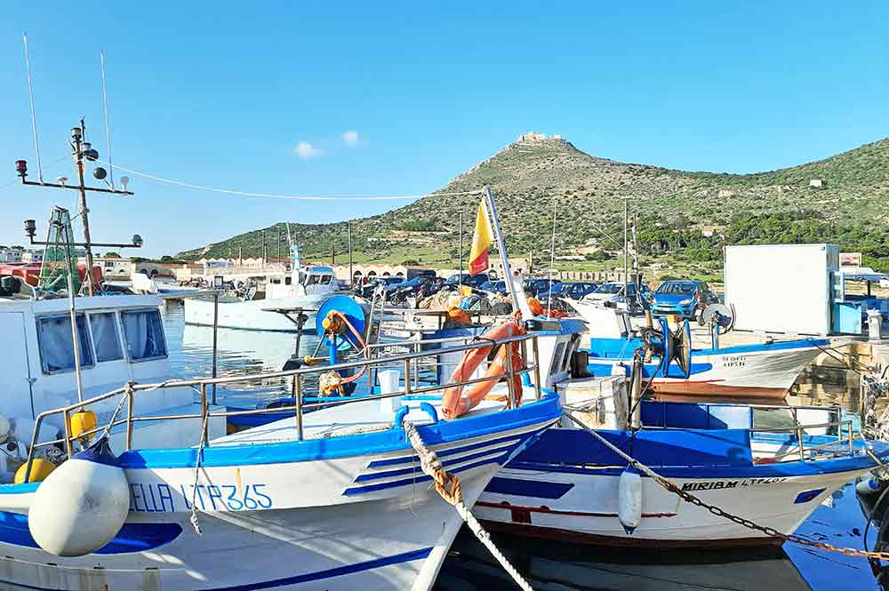 White and blue boats at Favignana Marina with castle on a hill in the background. 