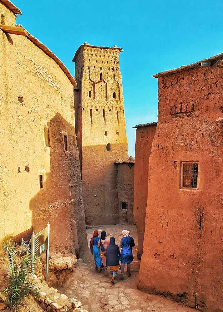 Travellers walking in the streets of Ait Ben Haddou with its ancient earthen architecture walls on shades of brown