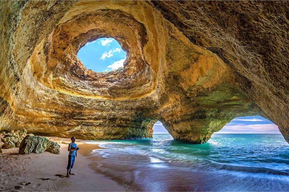 Benagil Cave, Portugal A sunlit sea cave with a circular skylight at the top that lets shafts of light pour in, illuminating a hidden sandy inlet and clear turquoise water—an unforgettable sight bathed in soft winter daylight in southern Europe.