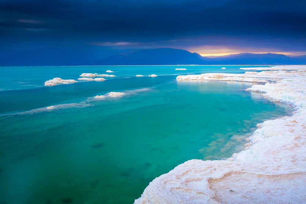 Turquoise waters and white salt formations of the Dead Sea at sunset, one of the most unique dream travel spots for wellness and nature enthusiasts.
