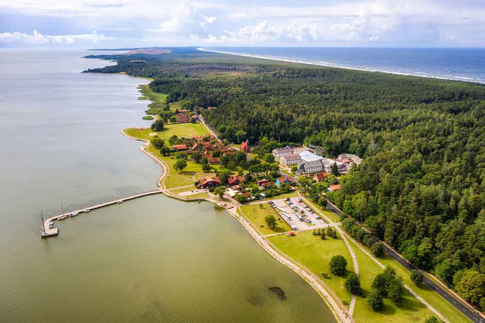 Best Of The Baltics: 23 Unmissable Things To Do In The Baltics 24 The aerial view of the Curonian Spit showcases stunning landscapes, houses, lush forest trees, and a long wooden pathway leading to the sea.