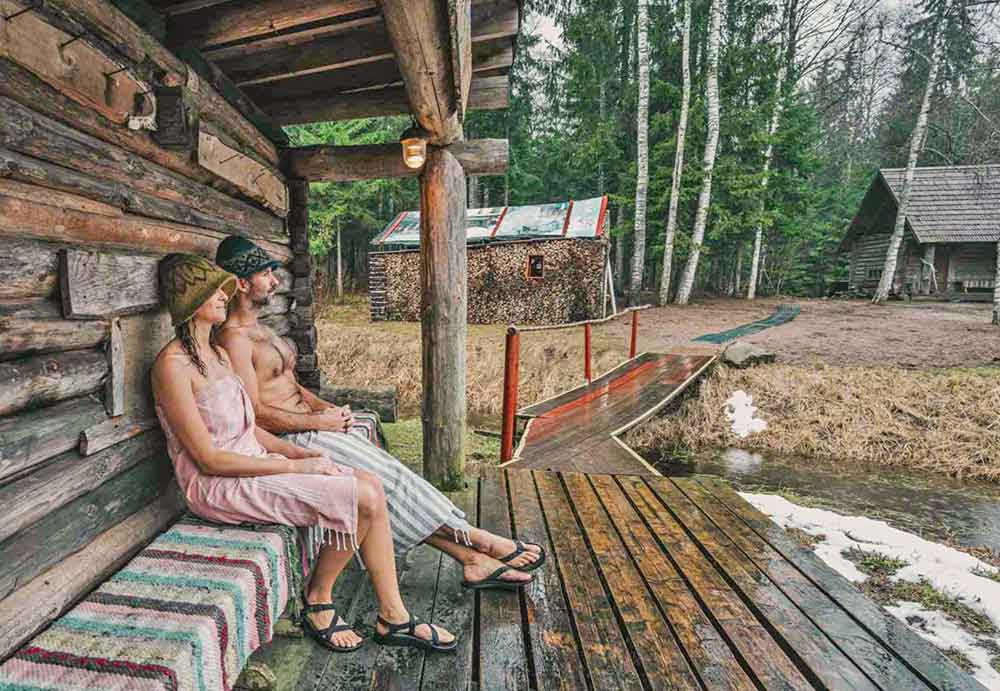 Best Of The Baltics: 23 Unmissable Things To Do In The Baltics 5 A couple sitting on the side of the house took a Mooska Farm Smoke Sauna in a charming log cabin surrounded by lush forests, meadows, and pristine nature.