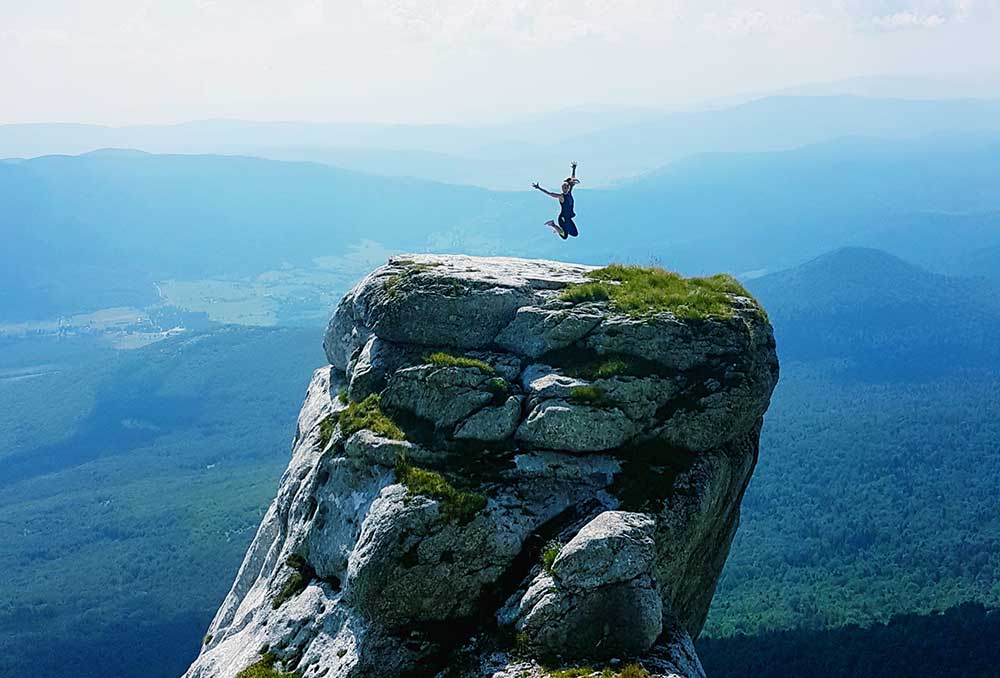 A woman take a jump shot on the top of the Croatia's most famous rock with a stunning view of mountains and forests