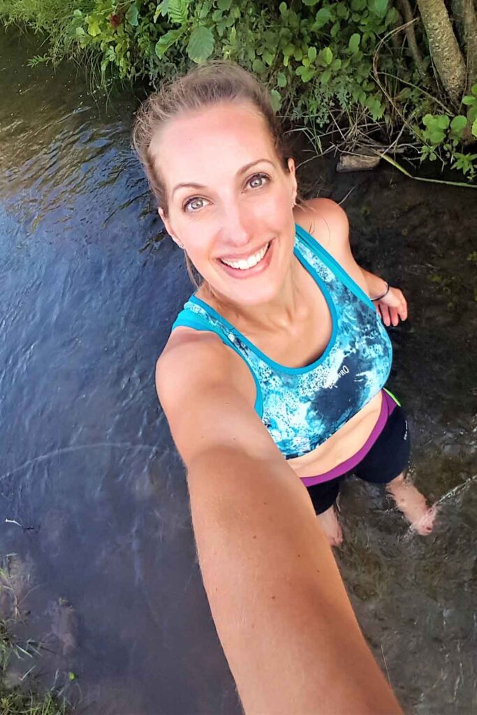 After the hike, a woman is taking a selfie while cooling her feet off in the river.
