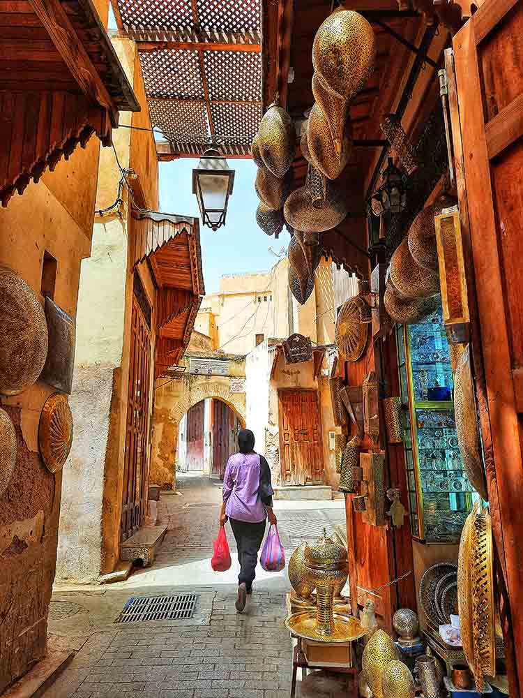 Woman walking down in the Souk of Fes feature the stalls of ornaments 