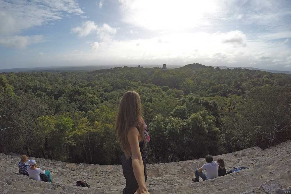 Woman taking a selfie while admiring the view of the jungle in a beautiful early morning sun around Tikal