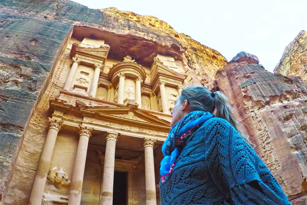 A woman (me) wearing a woolen poncho looking up at the Treasury in Petra