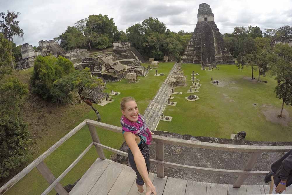 A woman is taking a selfie with The Grand Plaza in the background, featuring the temple of the Great Jaguar.