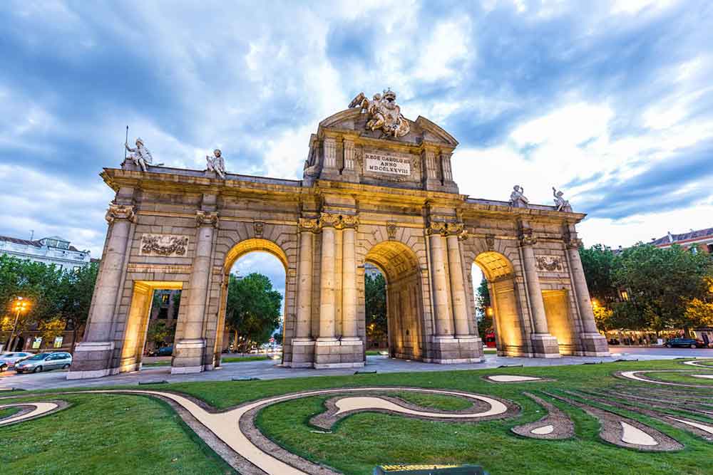 Puerta de Alcala features a five wide and segmented archways supported by columns adorned with intricate reliefs, figures and ornate details