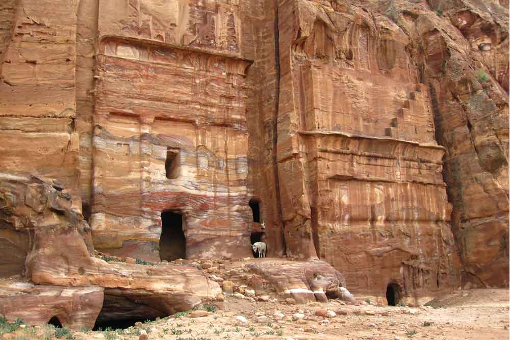 The Silk Tomb features high rock formations in a sand-colored hue with holes below.