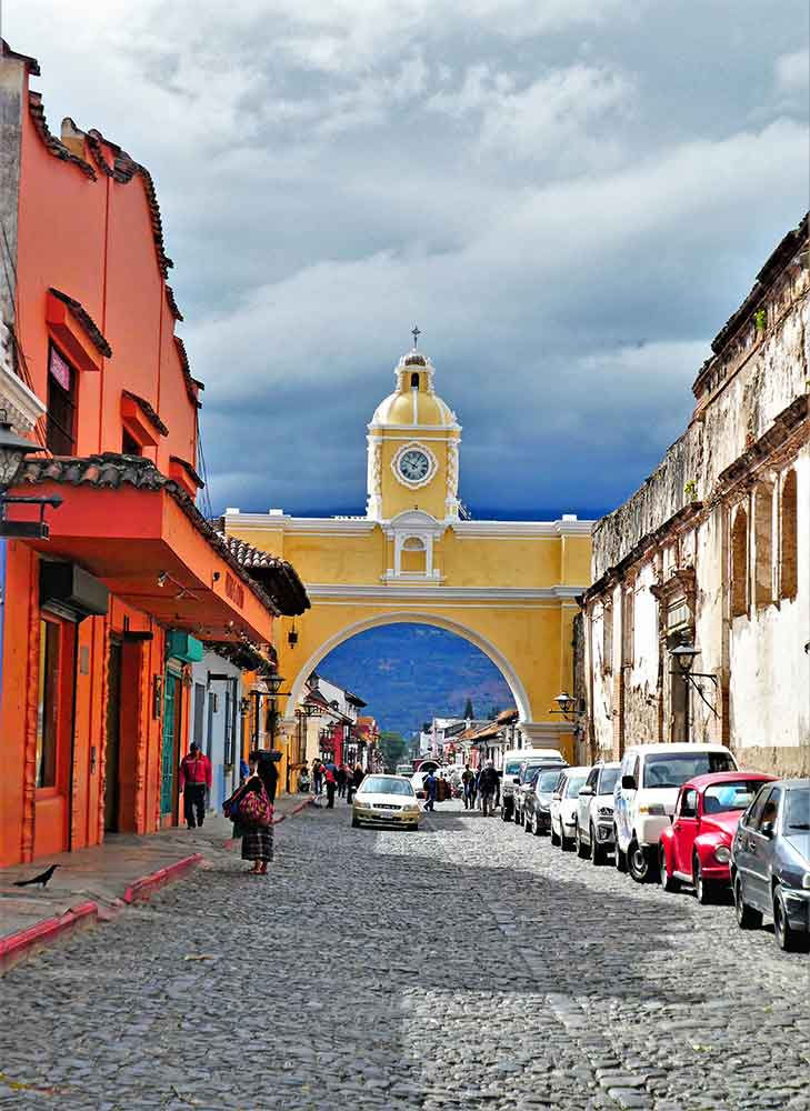 El Arco De Santa Catalina in Antigua features a yellow arch with a clock at the middle, surrounded by parked cars on the side, creating a beautiful blend of historical architecture and modern life