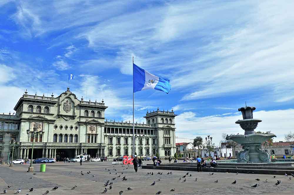 Palacio Nacional De La Cultura de Guatemala, a palace, features a gray-white facade adorned with columns, carved reliefs, and multiple windows with a fountain stands at the front